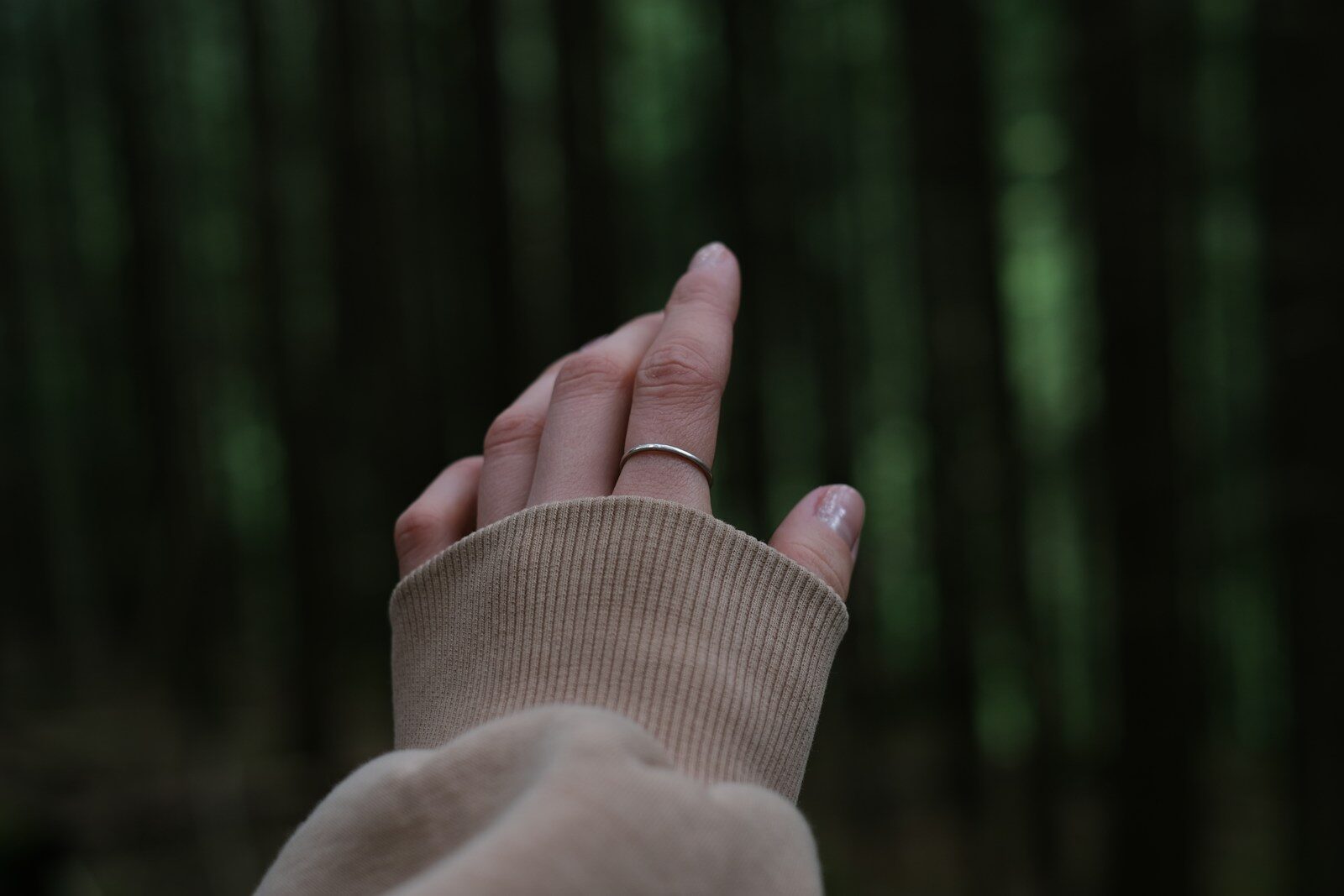 a woman's hand with a ring on it in front of a forest